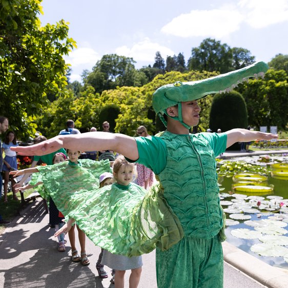 Ein Tänzer im Krokodilskostüm übt mit Kindern in der Wilhelma den Krokodilstanz ein