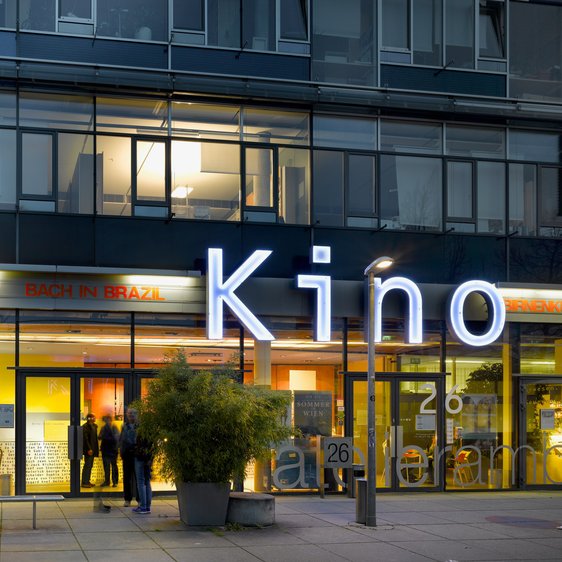 Ein Kino·gebäude ist zu sehen. Es ist hell beleuchtet. In großen Buchstaben steht Kino an der Wand.